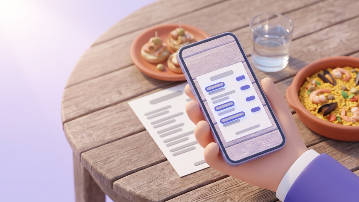A phone held over a wooden cafe table, its camera translating a printed menu, with a plate of tapas, a glass of water and a dish of paella nearby